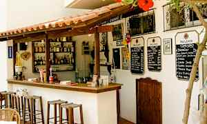 En liten utendørsbar med trestoler, drikkeflasker på hyllene og menyer på veggen. (AI-generert tekst)