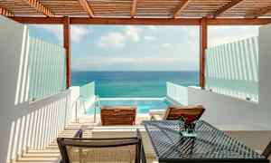 Utsikt over en terrasse med to solsenger, et bord og et privat basseng, med havet i bakgrunnen. (AI-generert tekst)