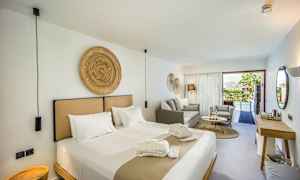 Et moderne hotellrom med en stor seng, sittegruppe og utsikt over et basseng gjennom glassdører. (AI-generert tekst)