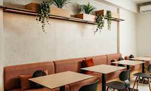 Et moderne kaféområde med røde sofaer og bord i tre, dekorert med plantekasser som henger over. (AI-generert tekst)