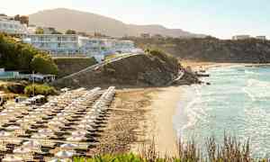 Strand med solsenger og parasoller, bygninger på skråningen. (AI-generert tekst)