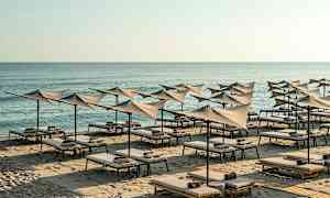 Strand med solsenger og parasoller ved sjøen. (AI-generert tekst)