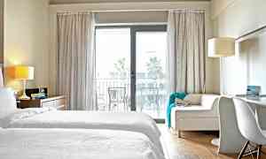 Et hotellrom med hvitt sengetøy og en sofa foran en glassdør til en balkong. (AI-generert tekst)