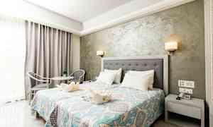 Et hotellrom med dobbeltseng, nattbord, dekorativt sengeteppe og sittegruppe. (AI-generert tekst)