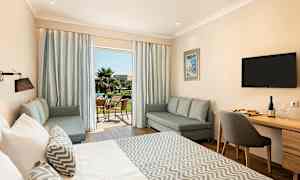 Et hotellrom med en stor seng, sittegruppe og et skrivebord. Terrassen er synlig gjennom glassdører. (AI-generert tekst)