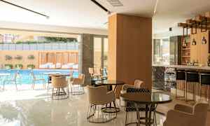 Et moderne kaféområde med sittegrupper, en bar og utsikt mot et svømmebasseng utenfor. (AI-generert tekst)