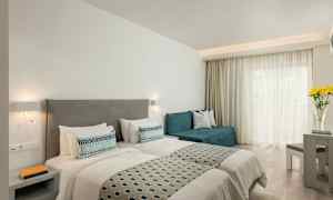 Et hotellrom med to enkeltsenger, en sofa, et bord og blomster på et bord ved et vindu. (AI-generert tekst)