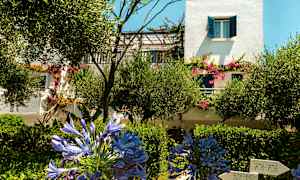 En hvit bygning med blå skodder og blomstrende planter i hagen. (AI-generert tekst)