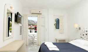 Et hotellrom med en seng, en TV på veggen og en balkong som viser utsikt over fjellene. (AI-generert tekst)