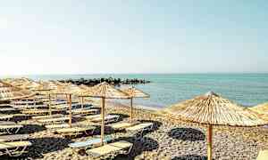 En strand med solsenger og parasoller foran et rolig hav. (AI-generert tekst)