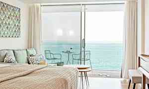 Et soverom med havutsikt gjennom store glassdører som fører til en balkong. (AI-generert tekst)