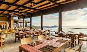 En åpen og lys restaurant med trebord og stoler, med utsikt over havet og horisonten. (AI-generert tekst)