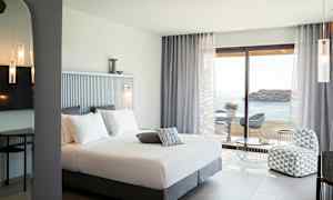 Hotellrom med dobbeltseng, sittegruppe og utsikt over havet. (AI-generert tekst)