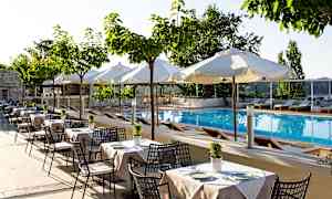 Bilde av et utendørs svømmebasseng med solsenger og hvite parasoller, omgitt av bord og stoler under små trær. (AI-generert tekst)