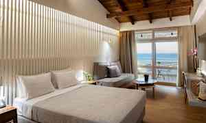 Hotellrom med dobbeltseng, sofa og balkong med havutsikt. (AI-generert tekst)