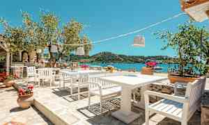 Uteservering med hvite stoler og bord, utsikt over havet og grønne åser. (AI-generert tekst)