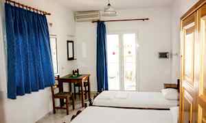 Et hotellrom med to enkeltsenger, et bord med stoler, blå gardiner og en balkongdør. (AI-generert tekst)