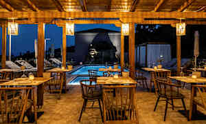 Utendørs servering med trestoler og bord, basseng og belysning om kvelden. (AI-generert tekst)