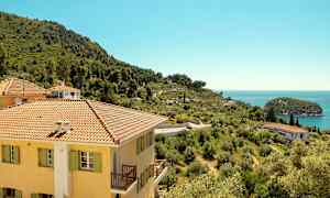 Bygning med gul fasade og skrått landskap med havutsikt. (AI-generert tekst)