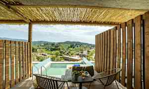 Terrasse med trevegger, bord og stoler, basseng og utsikt over landskapet med hus og grønne åser. (AI-generert tekst)