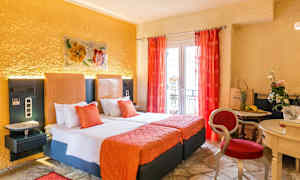 Et hotellrom med to senger, oransje interiør og røde gardiner, samt et lite bord med stoler og dekorasjoner. (AI-generert tekst)