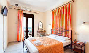Rom med dobbeltseng, oransje sengeteppe og gardiner, et speil og bord samt en balkongdør. (AI-generert tekst)