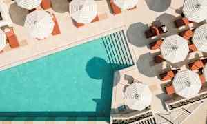 Et basseng med turkist vann omgitt av solsenger under stripete parasoller. (AI-generert tekst)
