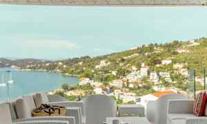 Utemøbler på en terrasse med utsikt over havet og en kystby. (AI-generert tekst)