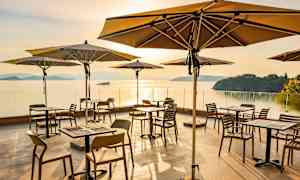 Uteservering med bord og parasoller ved havet i solnedgang. (AI-generert tekst)