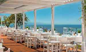 Utendørsrestaurant med hvite møbler og utsikt over havet. (AI-generert tekst)