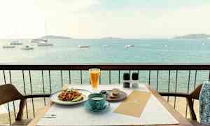 Utsikt over en tallerken med mat og en kopp kaffe plassert på et bord på en balkong med utsikt over havet. (AI-generert tekst)