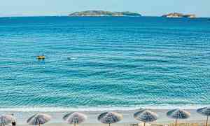 Strand med parasoller, hav og øyer i bakgrunnen. (AI-generert tekst)