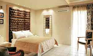 Et soverom med en dobbeltseng, en stor polstret sengegavl og et speil på veggen. (AI-generert tekst)