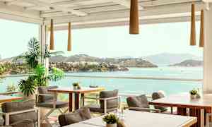 Uteservering med bord og stoler, samt utsikt over havet og frodige øyer. (AI-generert tekst)