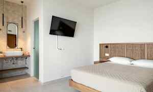 Hotellrom med en dobbeltseng, veggmontert TV og et åpent baderom. (AI-generert tekst)