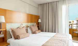 To senger i et hotellrom med lyse tekstiler og trematerialer. (AI-generert tekst)