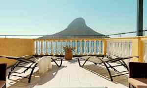 Terrasse med solsenger og utsikt over havet og en liten fjellformasjon. (AI-generert tekst)