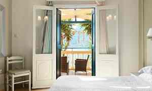 Et lyst soverom med åpne dører til en balkong med møbler og utsikt over havet. (AI-generert tekst)