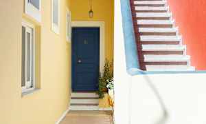 En blå dør med trinn og en gul vegg ved siden av en trapp med rødt veggparti. (AI-generert tekst)