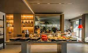 Bufféområde med ulike retter og drikkevarer på et bord. Bakgrunn med hyller og sitteplasser. (AI-generert tekst)