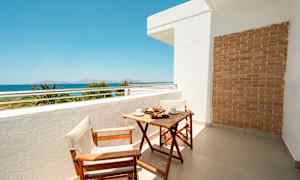 Balkong med trebord og to stoler, havutsikt i bakgrunnen. (AI-generert tekst)