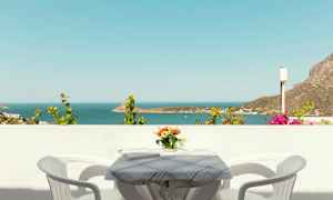 Utsikt over havet fra en balkong med et bord, to stoler og en vase med blomster. (AI-generert tekst)