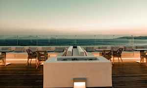 En terrasse med sitteplasser og bord med utsikt over havet ved solnedgang. (AI-generert tekst)