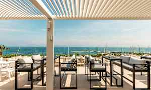 Utendørs servering med utsikt over havet, med sofaer og bord under en pergola. (AI-generert tekst)