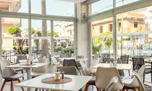 En lys restaurant med vinduer ut mot gaten og utendørsbord. (AI-generert tekst)