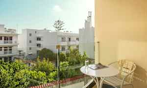 Balkong med bord og stol, utsikt over hvite bygninger og grøntområder. (AI-generert tekst)