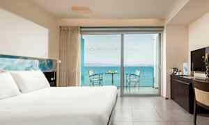 Et hotellrom med en stor seng, et skrivebord og en balkong med havutsikt. (AI-generert tekst)