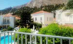 Bildet viser et utendørsområde med svømmebasseng, bygninger og en fjellandskap i bakgrunnen. (AI-generert tekst)