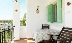 Balkong med to stoler og et bord, grønn vindusluker og veggdekorasjon. (AI-generert tekst)