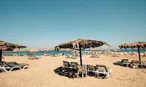 Strand med solsenger og parasoller laget av halmtak. (AI-generert tekst)